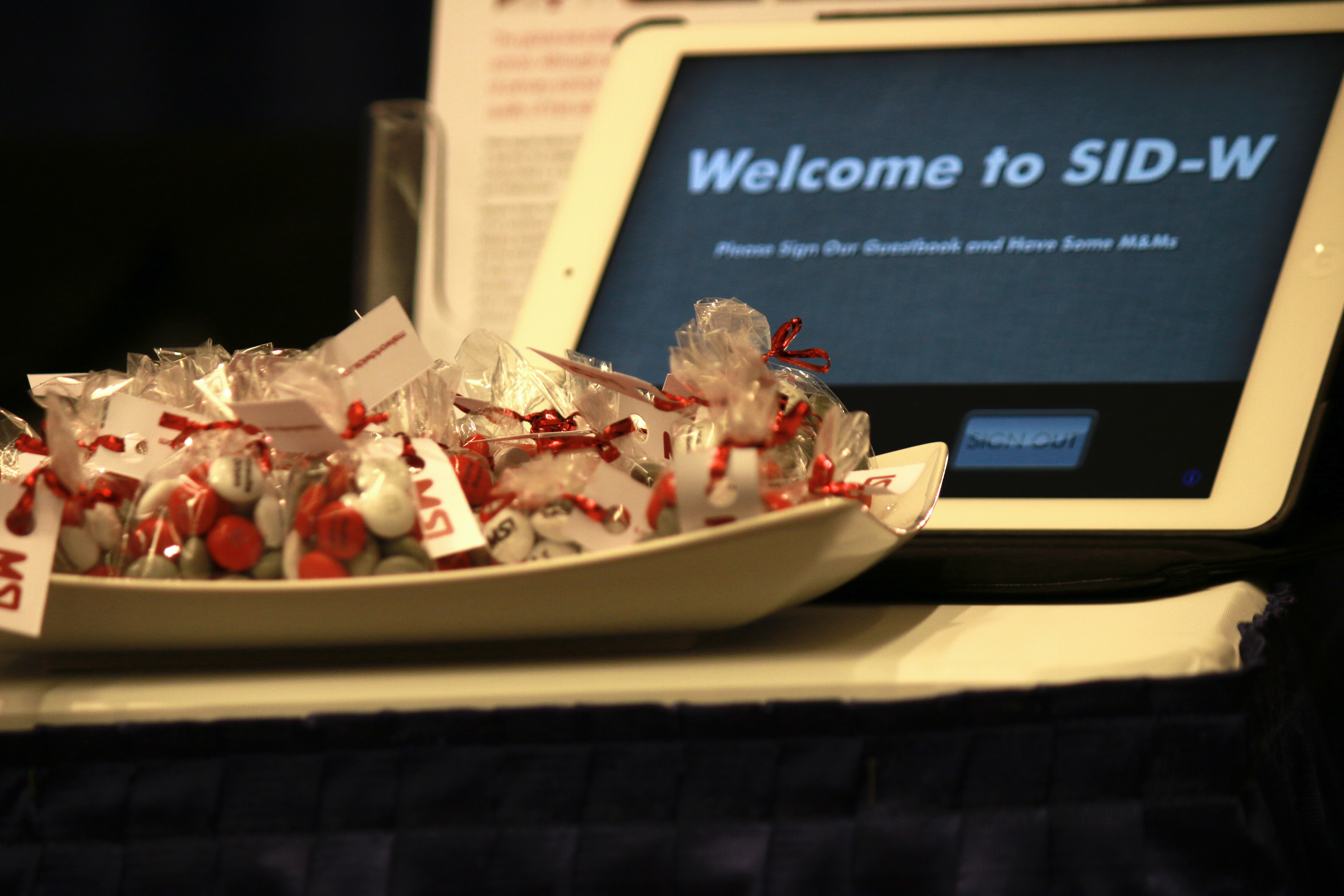 Bowl of MSI-branded M&M candies sits in front of iPad that reads "Welcome to SID-W"