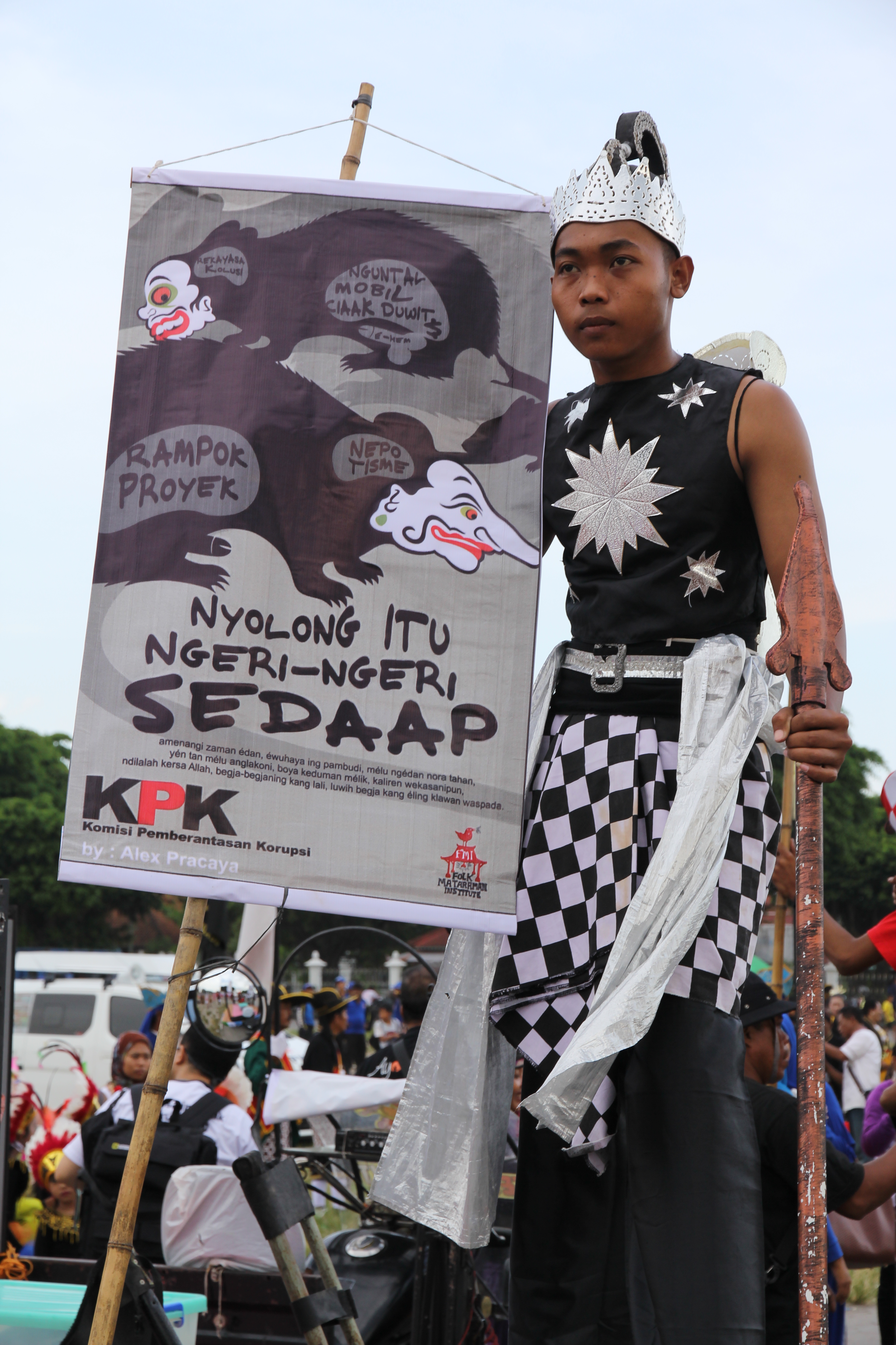 Man in traditional garb holding sign during anti-corruption protest in Indonesia.
