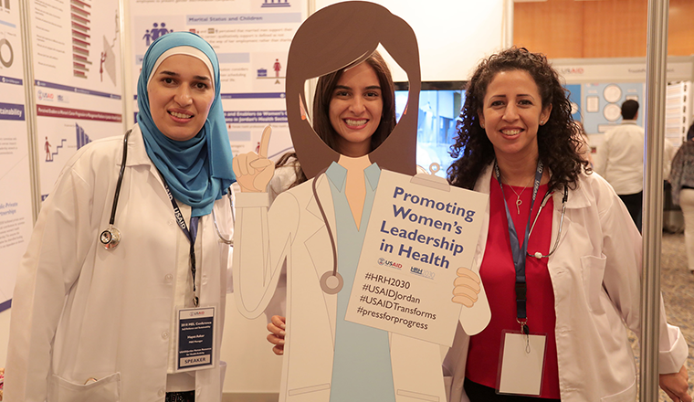 Three women with sign reading - Promoting Women' Leadership in Health
