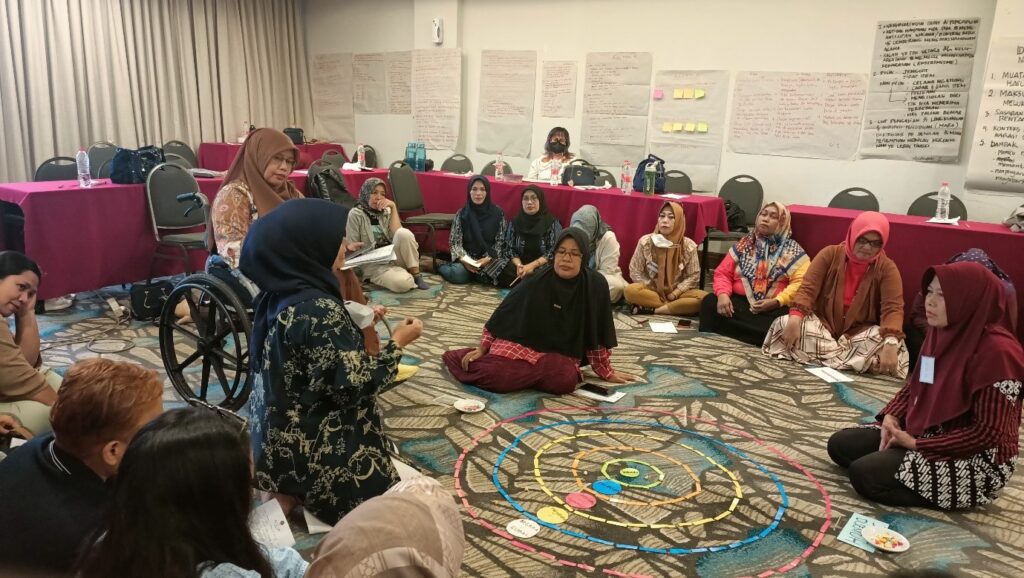 Several Indonesian women sit in a circle on the floor during a training exercise.